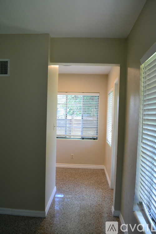 A hallway with a window and blinds leading to another room.