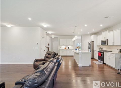 A modern living room with a row of leather chairs facing a kitchen.