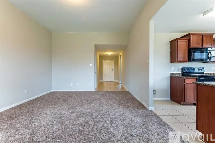 A spacious living room with a carpeted floor and a kitchen area with brown cabinets and appliances.