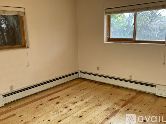 A room with wooden flooring and a window with a view of trees.