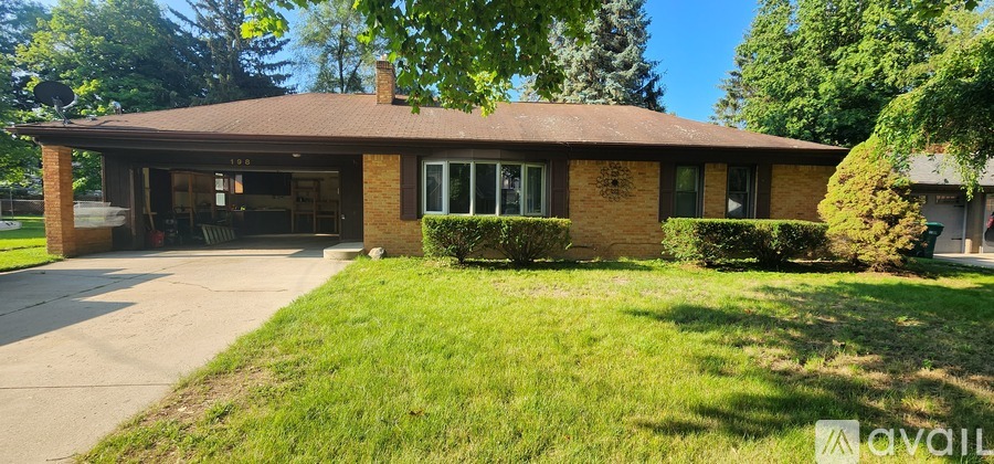 A house with a brown roof and a garage is surrounded by green grass and trees.