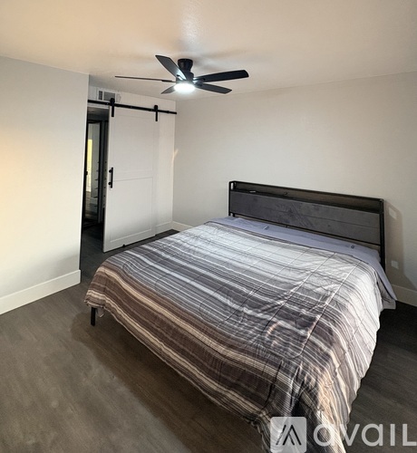 A bedroom with a bed, ceiling fan, and a door.