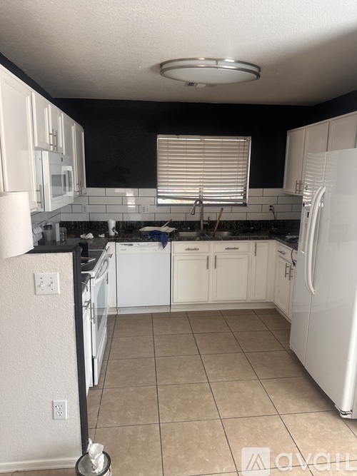A kitchen with white appliances and black countertops.