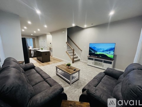 A living room with a black leather sofa and a television on the wall.