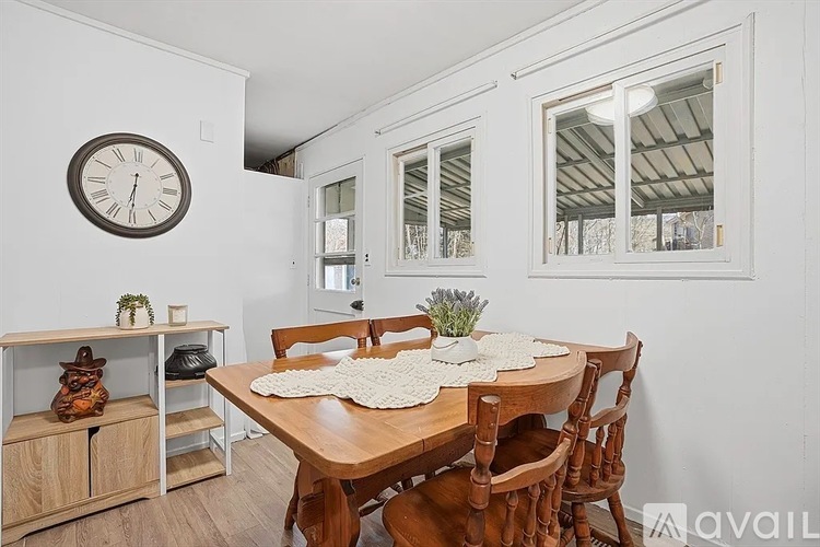 A dining room with a wooden table and chairs, a clock on the wall, and a cabinet with a plant on top.