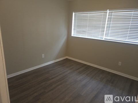 A room with a window covered by white blinds and wooden flooring.