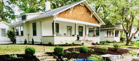 A white house with a brown roof and a garden in front.