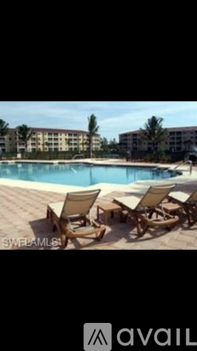 A pool with chairs around it and a building in the background.