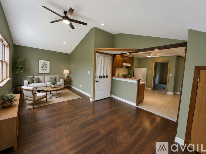 A living room with a ceiling fan and a kitchen in the background.