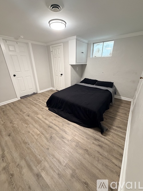 A bedroom with a bed, wooden flooring, and white walls.