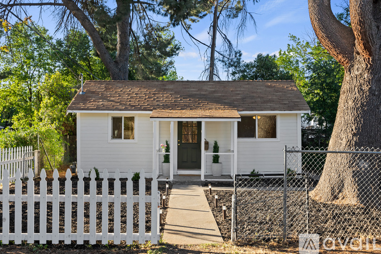 A small white house with a brown roof and a white picket fence.