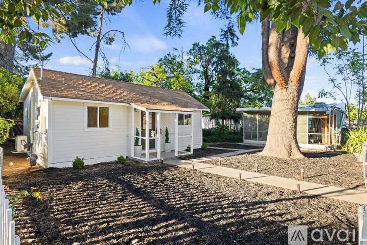 A white house with a brown roof is surrounded by trees and has a gravel driveway.
