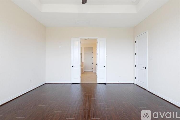 A room with white walls and wooden flooring, with a doorway leading to another room.