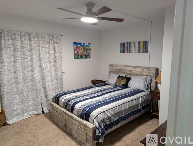 A bedroom with a bed, a ceiling fan, and a painting on the wall.