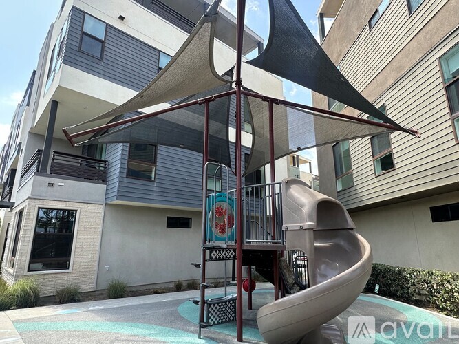 A playground with a slide and a canopy is located in front of a building.