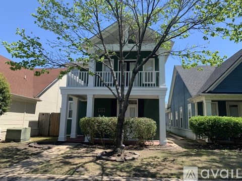 A tree in front of a house with a porch.