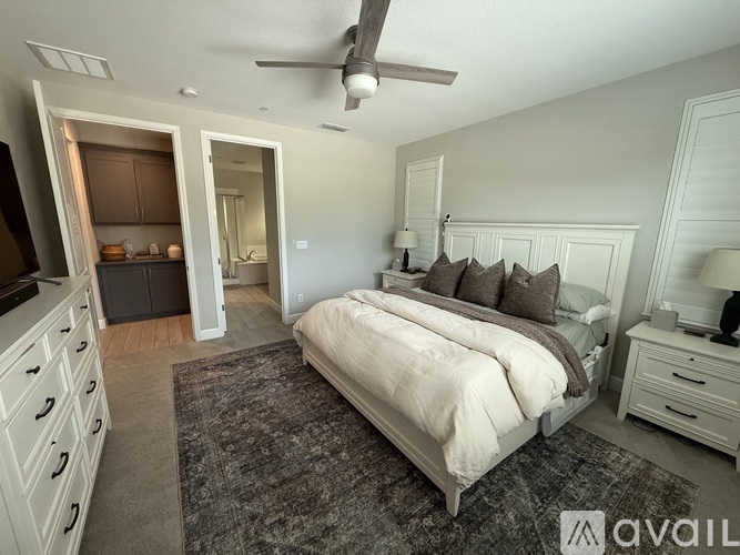 A bedroom with a large bed, a ceiling fan, and a kitchen area with a refrigerator and cabinets.