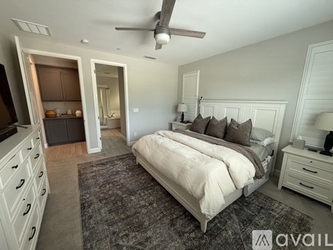 A bedroom with a large bed, a ceiling fan, and a kitchen area with a refrigerator and cabinets.