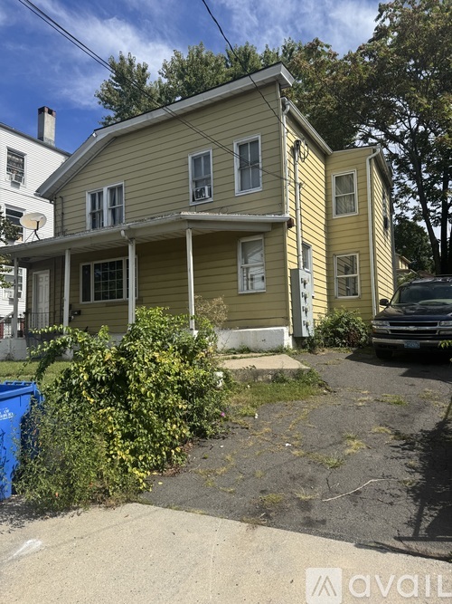 A yellow house with a blue trash bin in front of it.