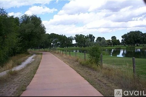 A paved walkway leads through a grassy area with a body of water in the distance.