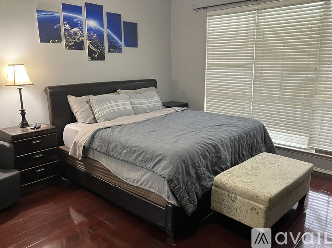 A bedroom with a large bed, a nightstand with a lamp, and a window with blinds.