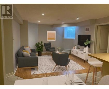 A living room with a grey couch, a black chair, a white coffee table, and a TV on the wall.