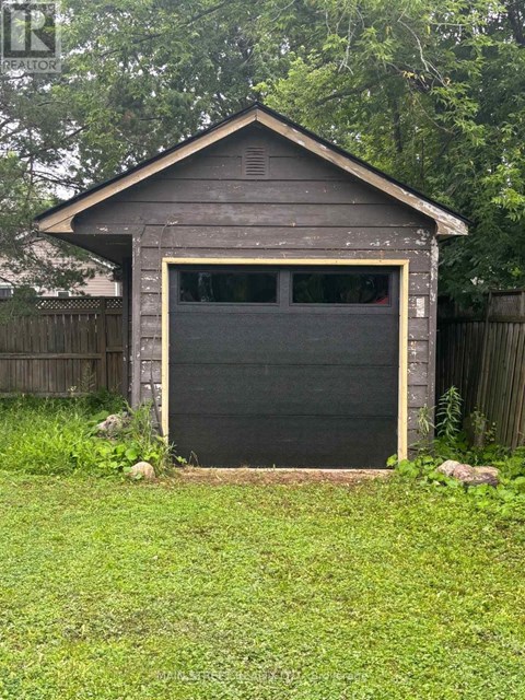 A small wooden garage with a black door is surrounded by a grassy area and a wooden fence.