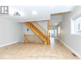A spacious room with a wooden staircase and tiled floor.