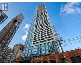 A tall building with a glass facade stands in front of other buildings.