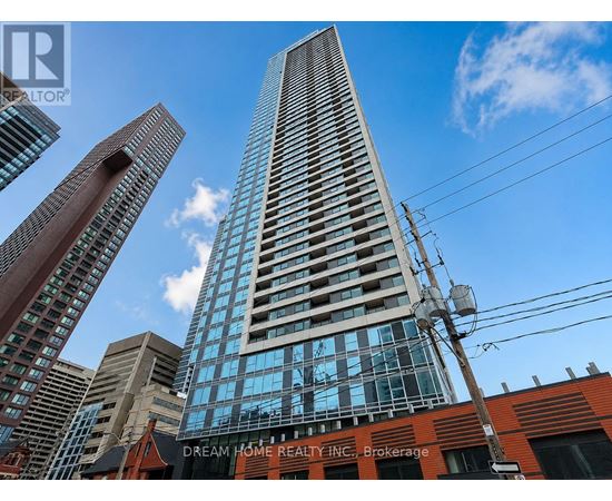 A tall building with a glass facade stands in front of other buildings.