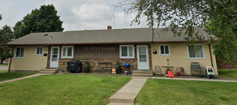 A small house with a porch and a tree in front.