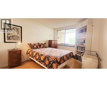 A bedroom with a bed, a nightstand, a chair, and a bookshelf.