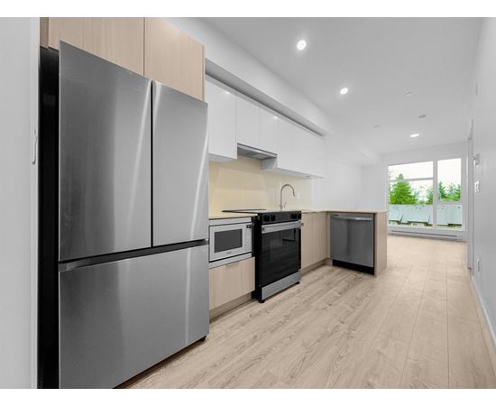 A modern kitchen with a stainless steel refrigerator and wooden flooring.