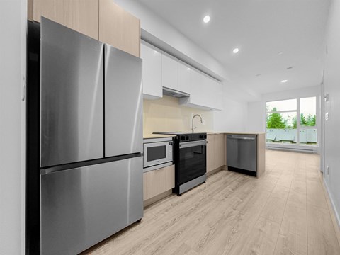 A modern kitchen with a stainless steel refrigerator and wooden flooring.