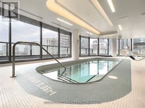 A modern indoor swimming pool with a glass bottom and a metal railing.