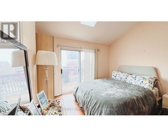 A bedroom with a bed, a nightstand, a lamp, and a window with a view of a city street.