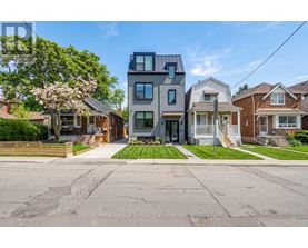 A modern two-story house with a grey exterior stands in front of a row of older houses.