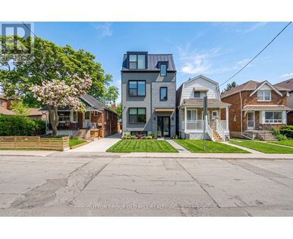 A modern two-story house with a grey exterior stands in front of a row of older houses.