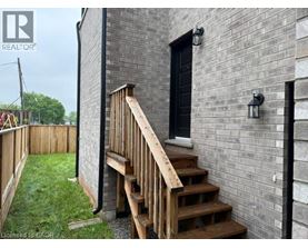 A wooden staircase leads up to a black door on a grey brick building.