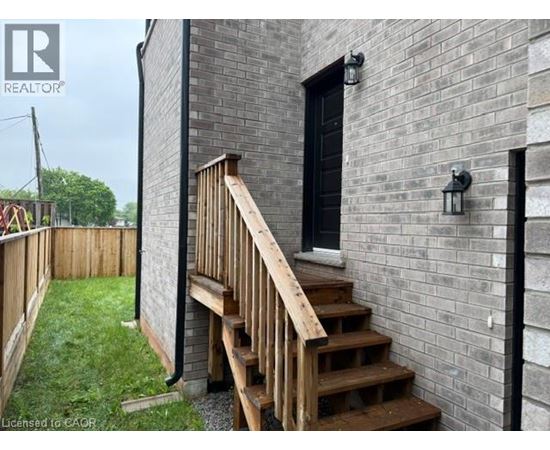 A wooden staircase leads up to a black door on a grey brick building.