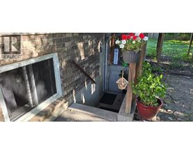 A flower pot with red and white flowers is hanging on a wooden post outside a building.