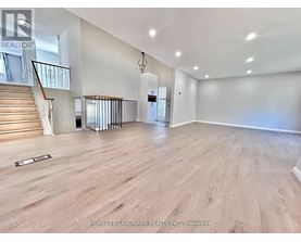 A spacious room with wooden flooring and a staircase with a metal railing.