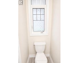 A white toilet in a bathroom with a window above it.