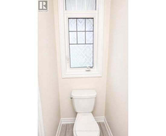 A white toilet in a bathroom with a window above it.