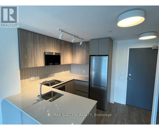 A modern kitchen with a stainless steel refrigerator and a flat screen TV mounted above the cabinets.