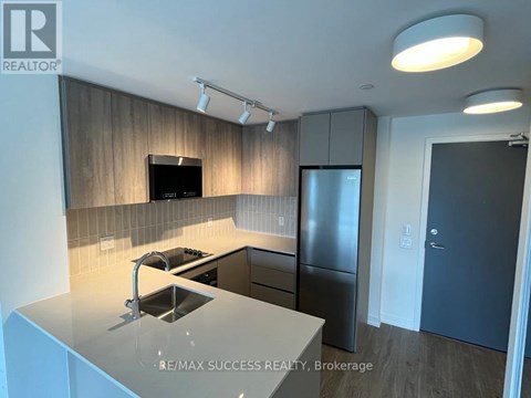 A modern kitchen with a stainless steel refrigerator and a flat screen TV mounted above the cabinets.