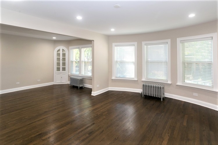 A room with wooden floors and three windows with blinds.