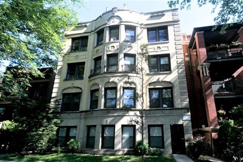 A large, old building with many windows is surrounded by trees.