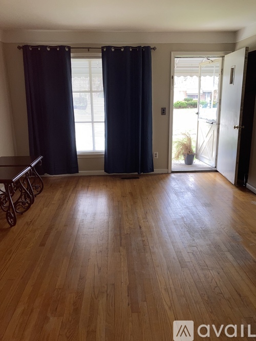 A room with wooden flooring and a window with dark curtains.