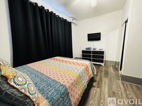 A bedroom with a bed covered in a multicolored quilt and a black curtain.